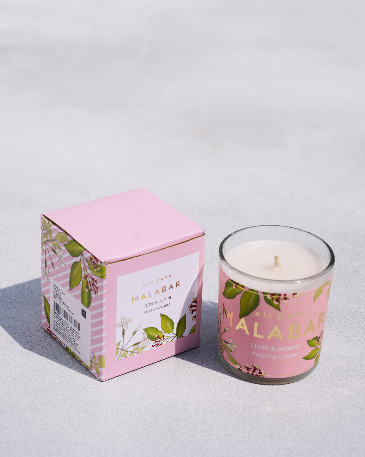 Malabar Jar Candle in pink glass with a clove and jasmine label, beside its box.