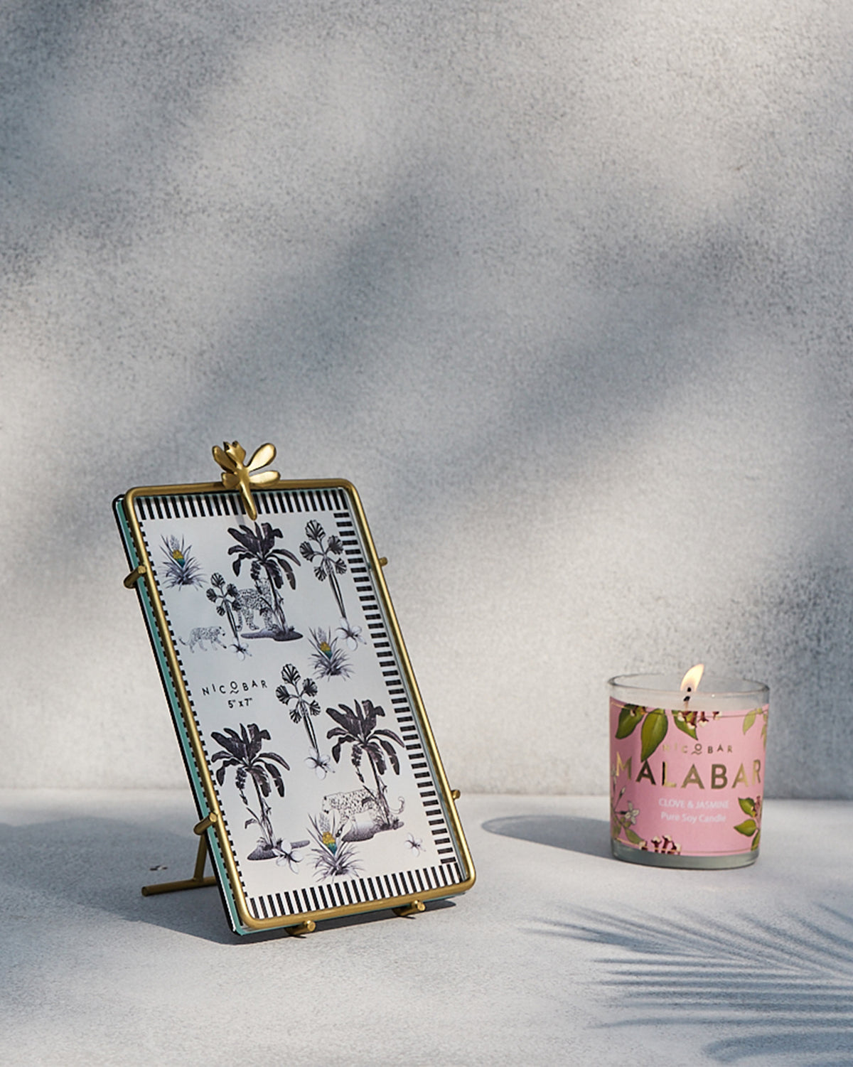 Lit Malabar Jar Candle beside a framed palm print.