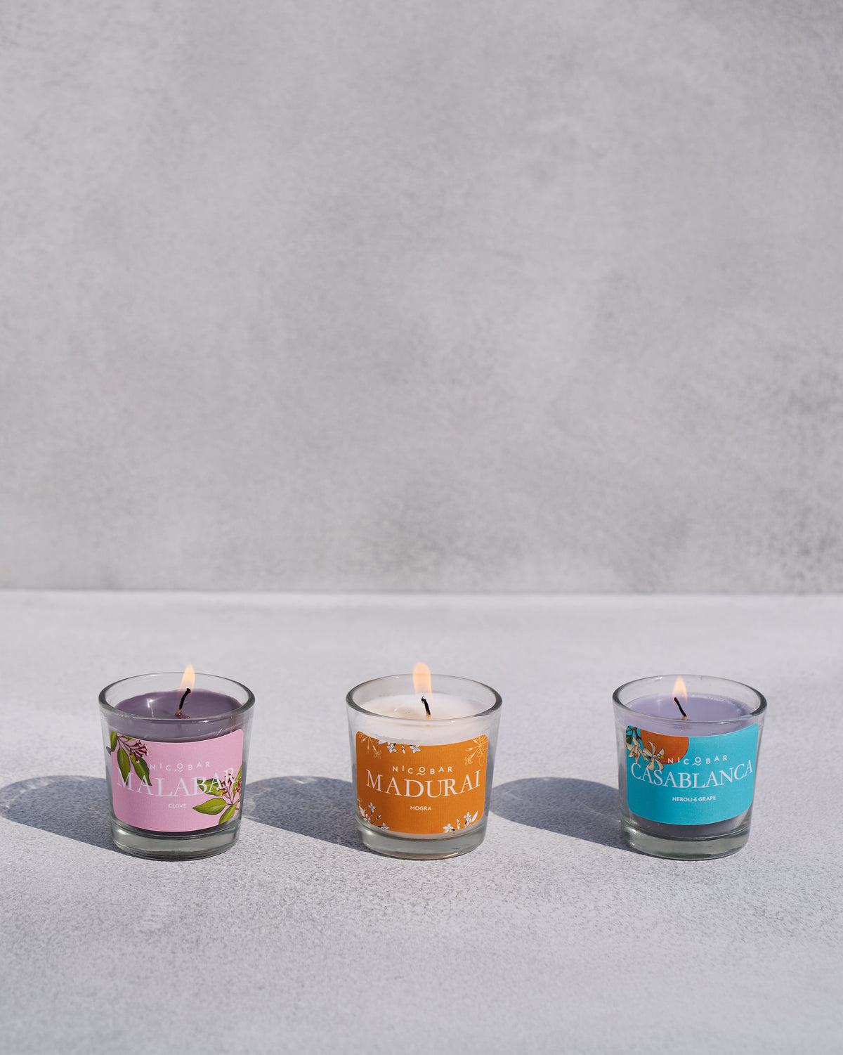 Three lit Trio Candle votives for Malabar, Madurai, and Casablanca scents.