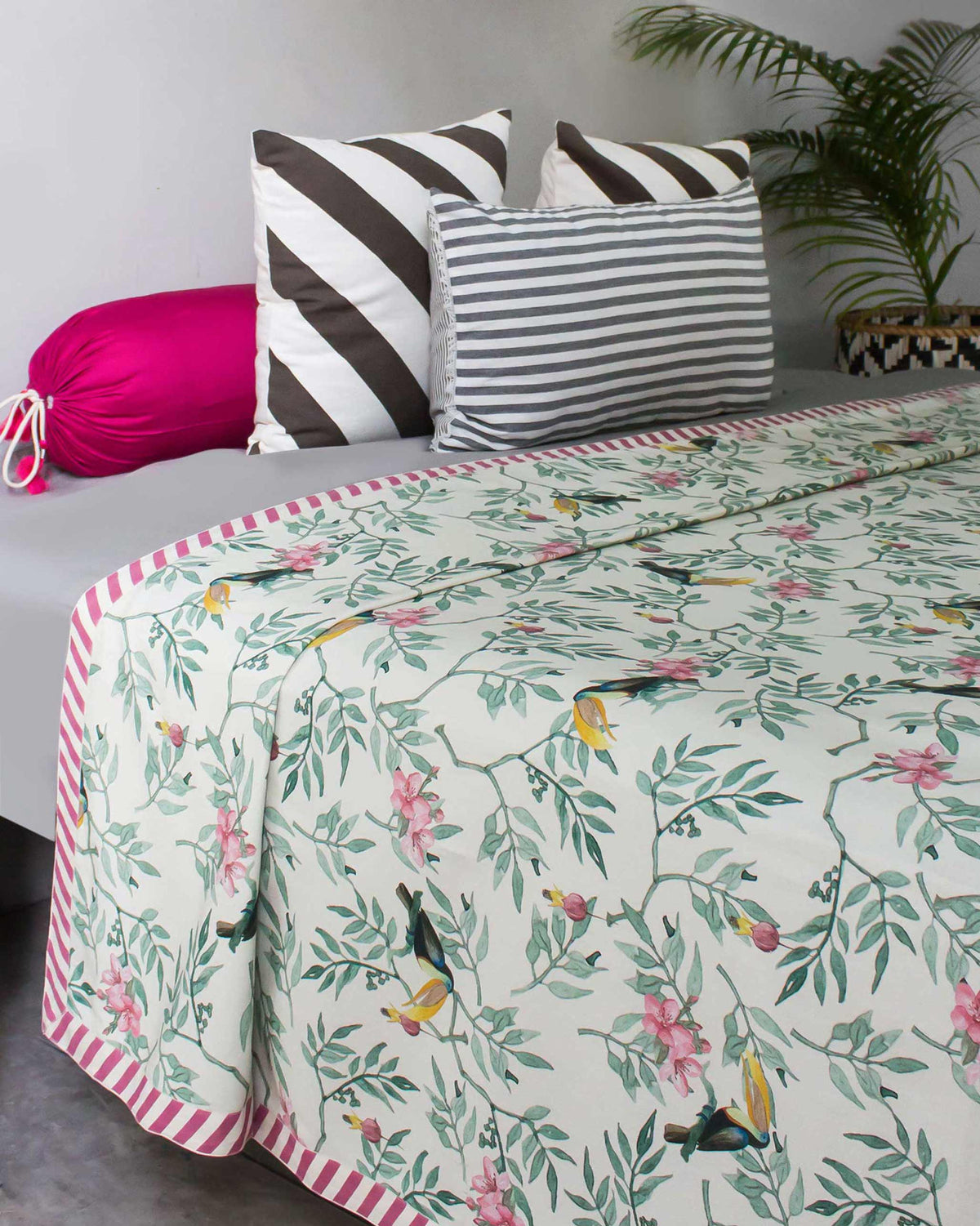 Nakano queen bed cover with toucan print styled with pink and striped cushions.