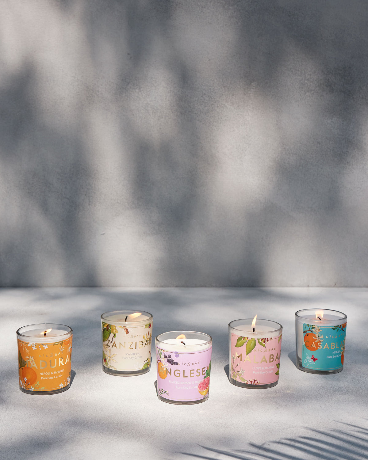 Five lit Nicobar jar candles lined up with colourful scent labels.