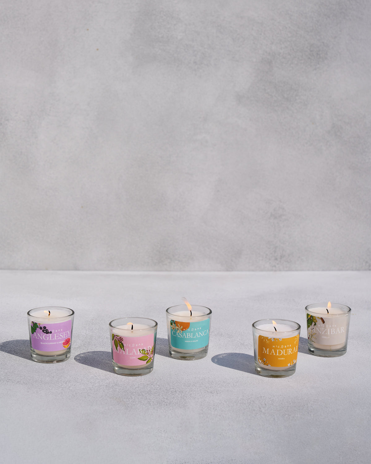 Five lit Nicobar jar candles arranged in an arc with scent labels.