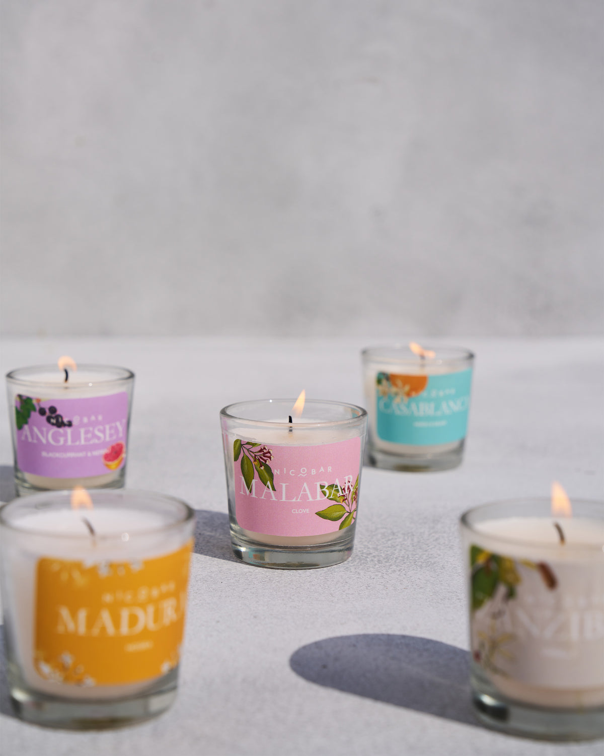 Five lit Nicobar jar candles clustered with colourful scent labels.