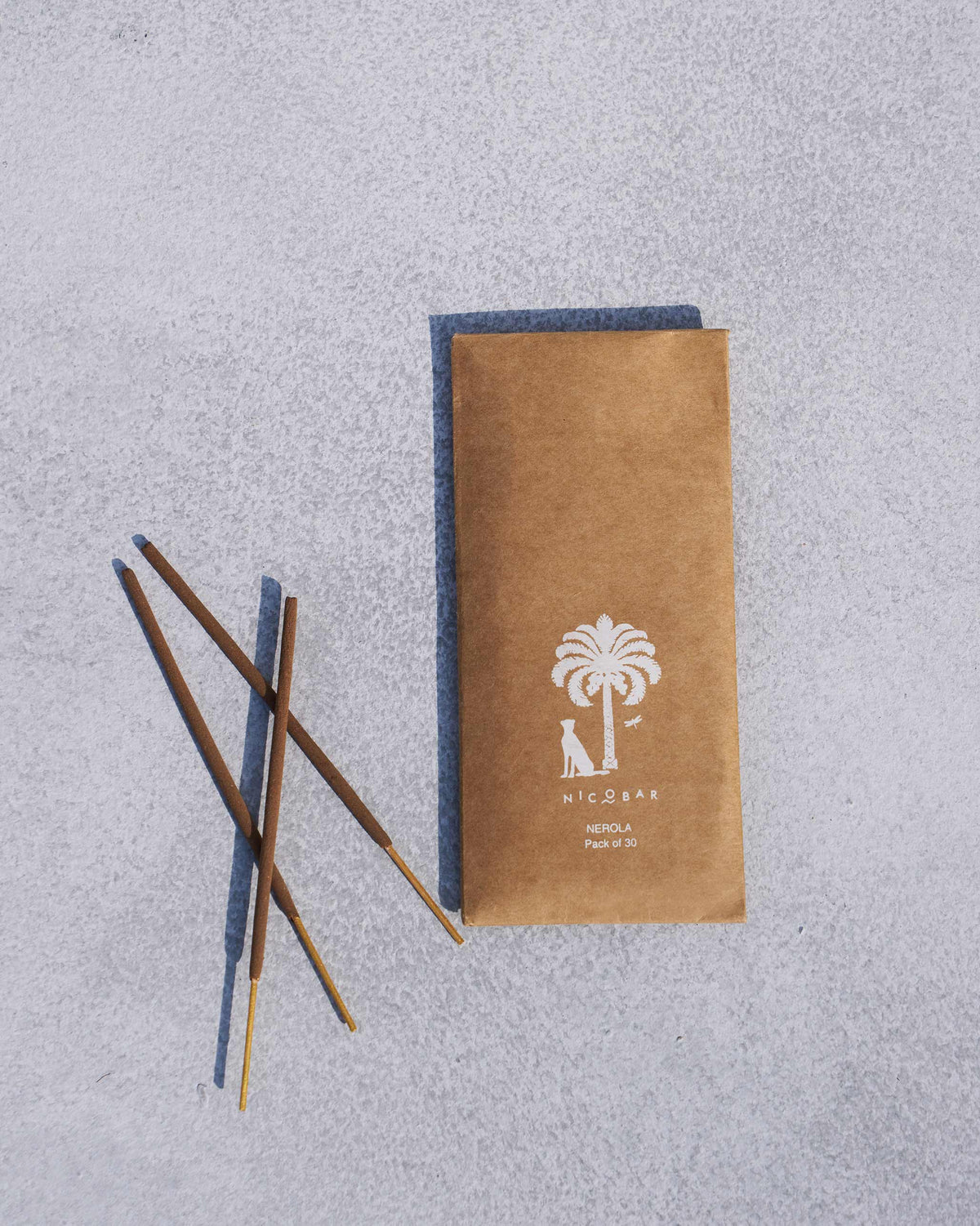 Madurai incense sleeve beside three dark brown sticks with pale wood ends.