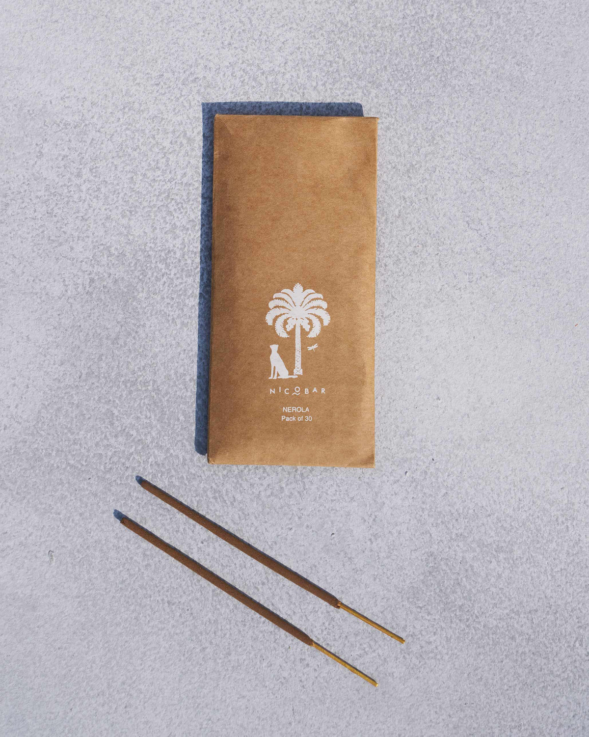 Madurai kraft incense pack with two loose sticks laid below on stone.