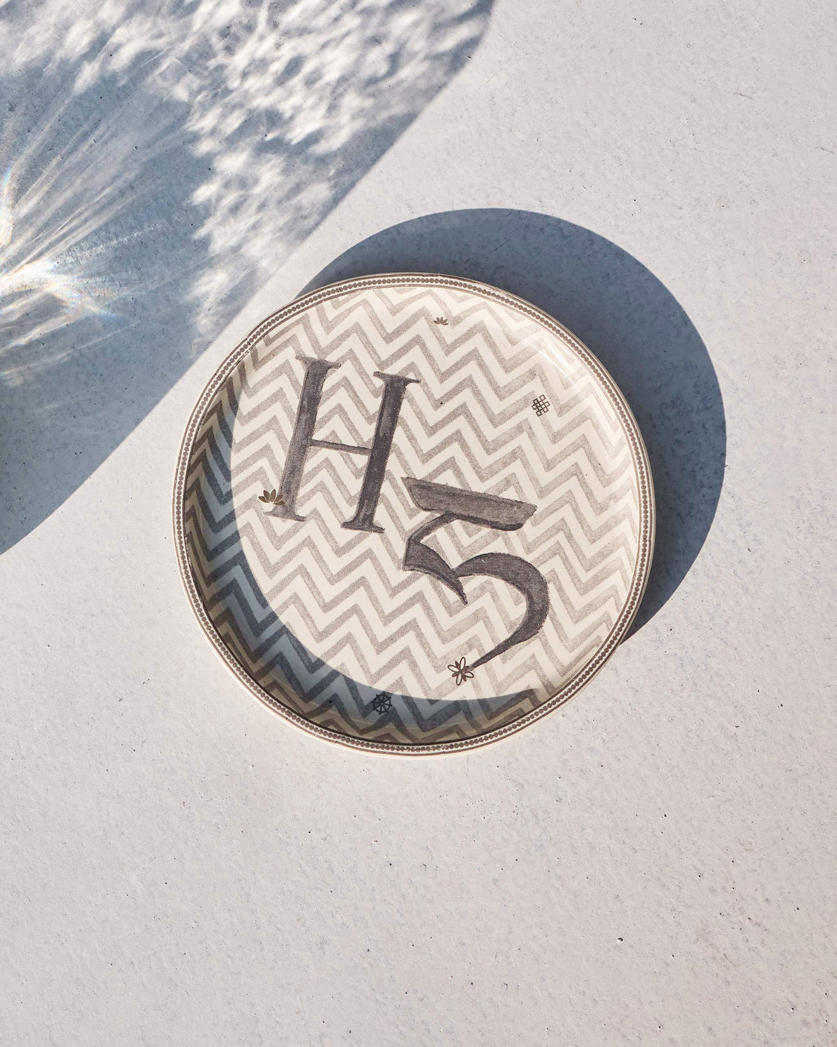Akshar Coaster with a letter H on a grey chevron pattern.