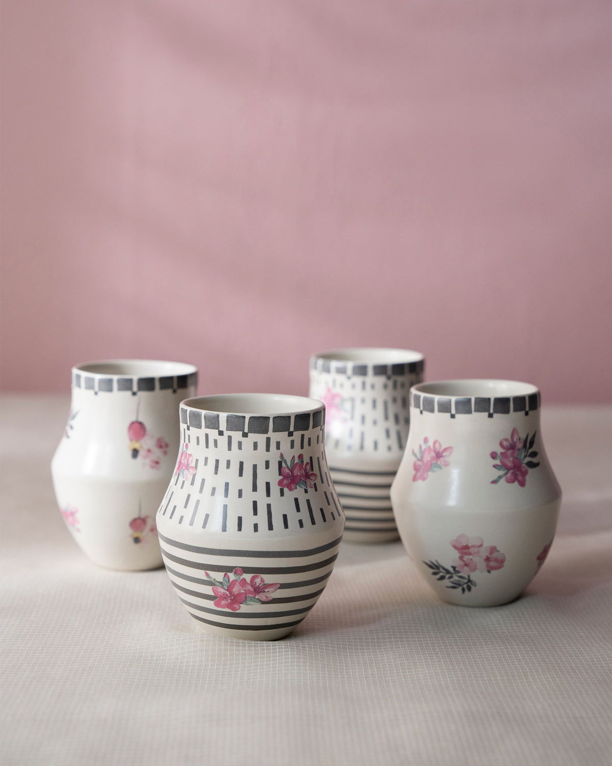 Four Nectar Kulhars standing in a row, with pink flower and stripe motifs.
