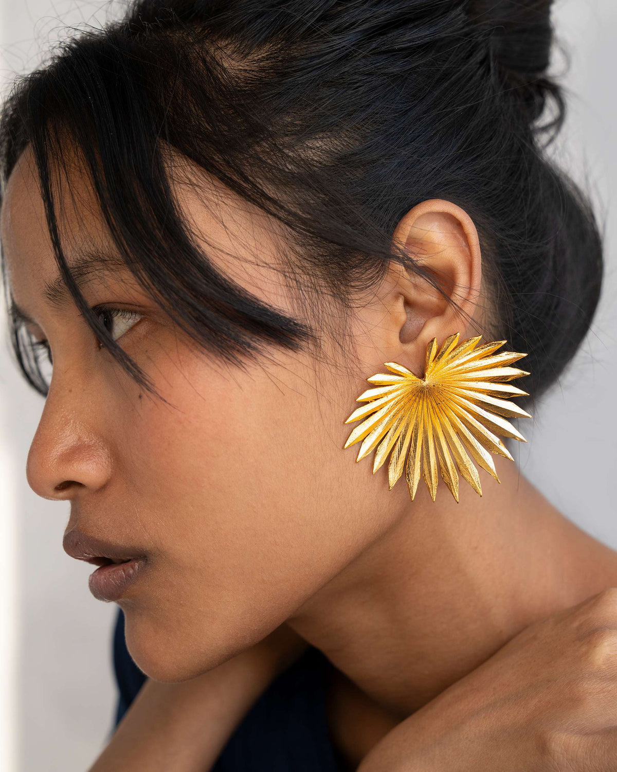 Side profile of gold palm leaf earrings on a person.
