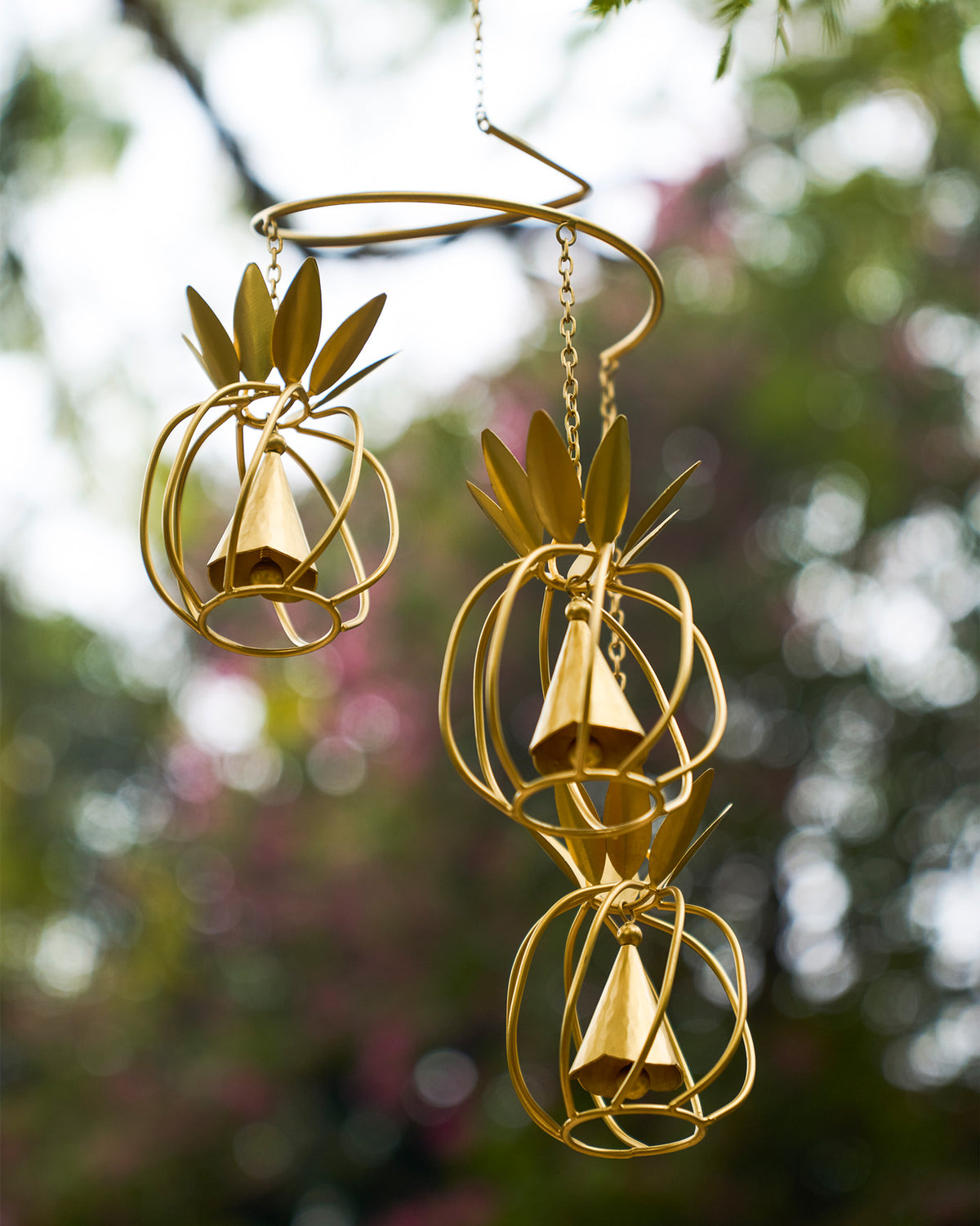 Gold pineapple wind chime hanging outdoors with three wireframe pineapple bells.
