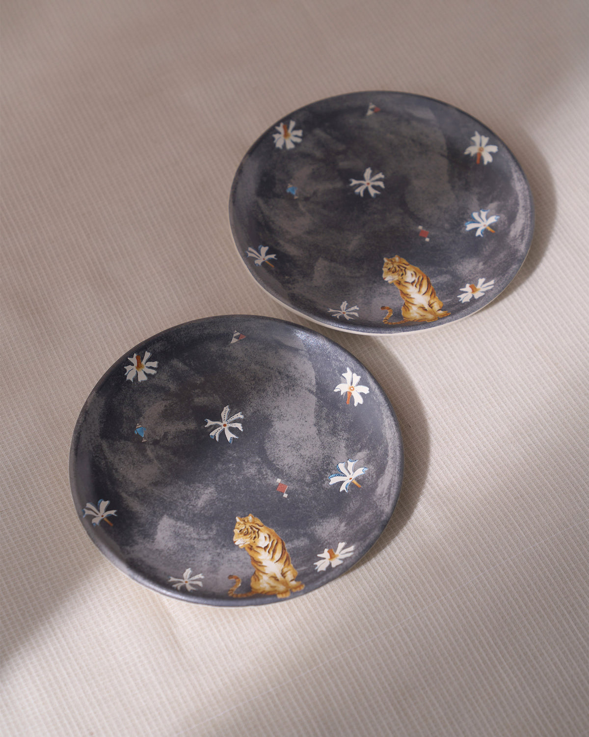 Pair of charcoal Nadi quarter plates with sitting tiger and white flower prints.