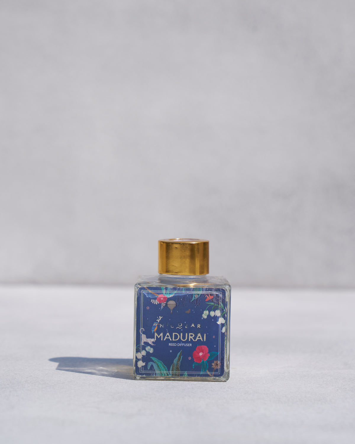 Madurai Reed Diffuser in a glass bottle with a blue floral label and gold cap.