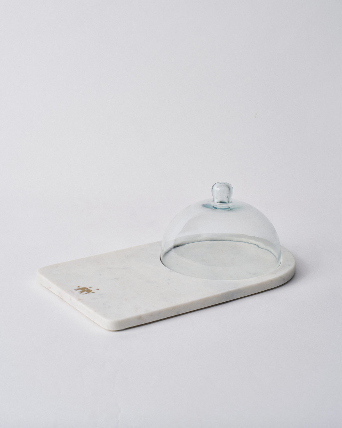White marble Ele cheese cloche with a clear glass dome and gold elephant motif.