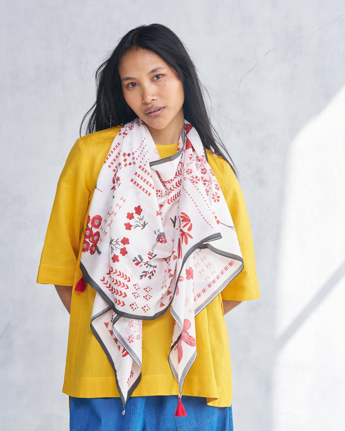 Person wearing a white Sugato scarf with red floral and geometric motifs.
