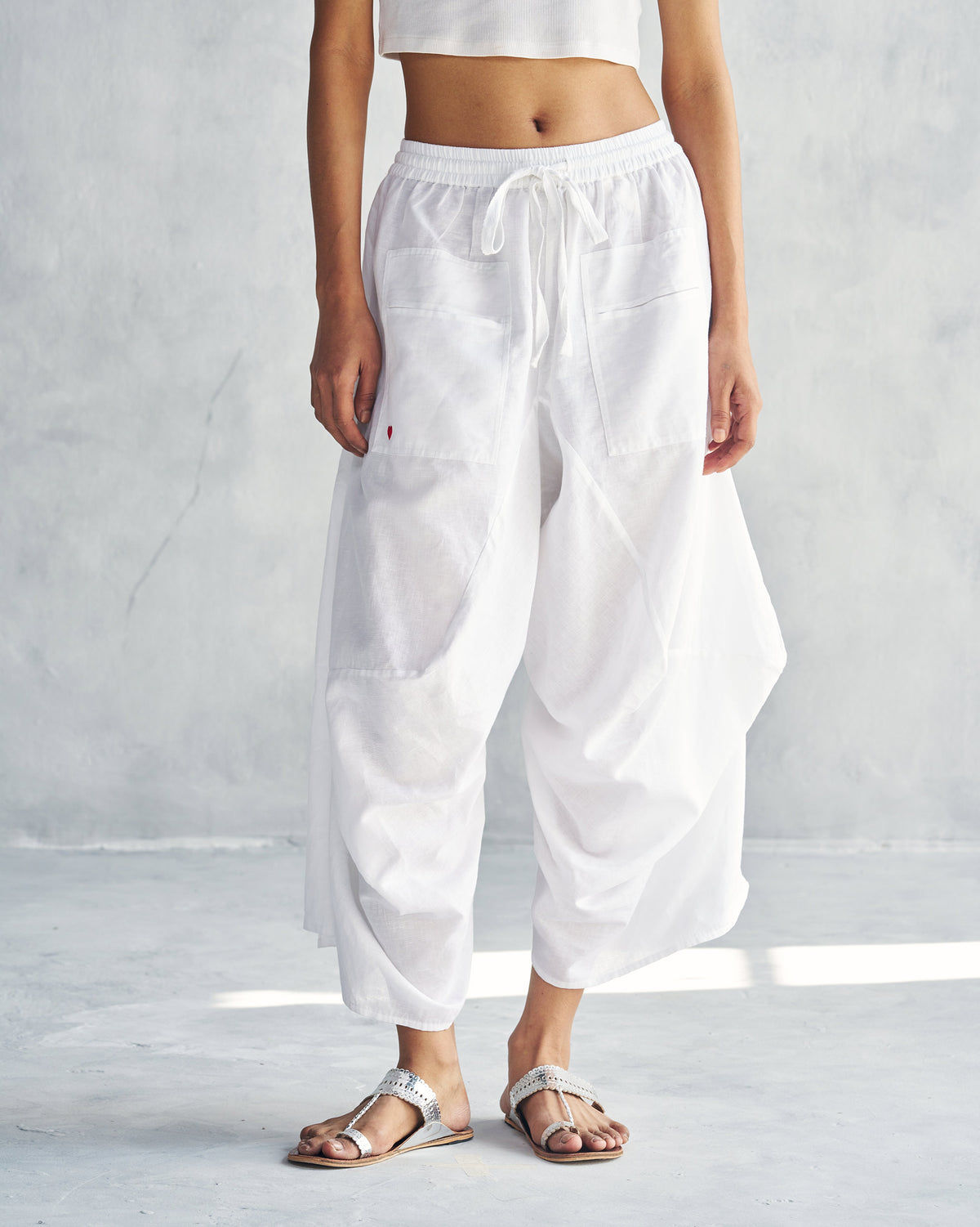 Person wearing white Yoka Trousers with a drawstring waist and patch pockets.
