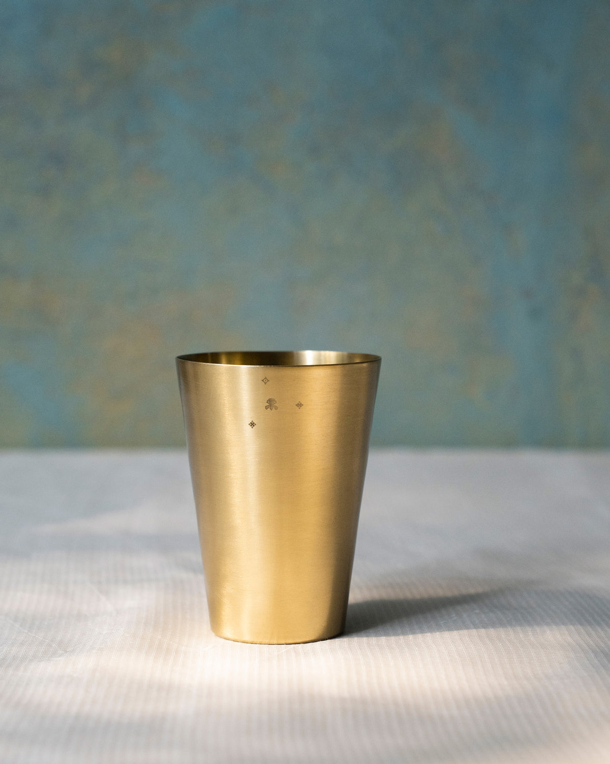 Brushed brass Madhu glass with a small stamped motif near the rim.