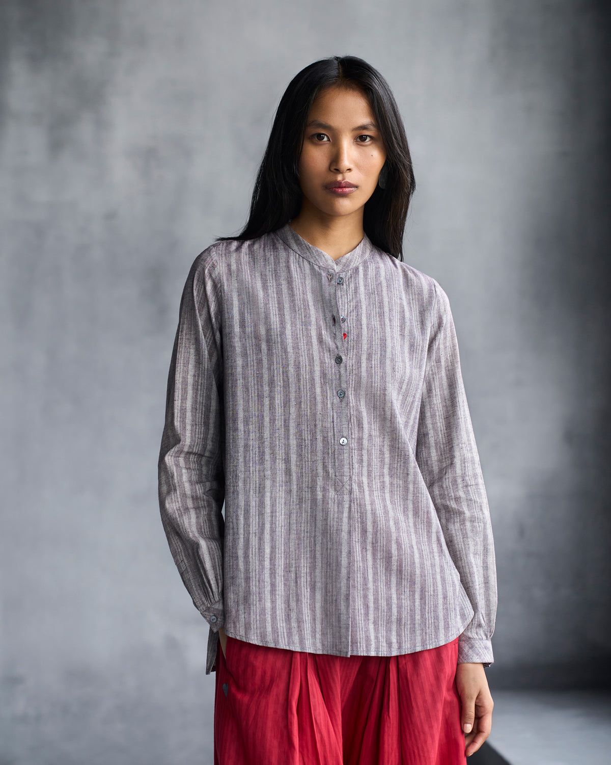 Person wearing a grey striped mandarin collar top with a short button placket.