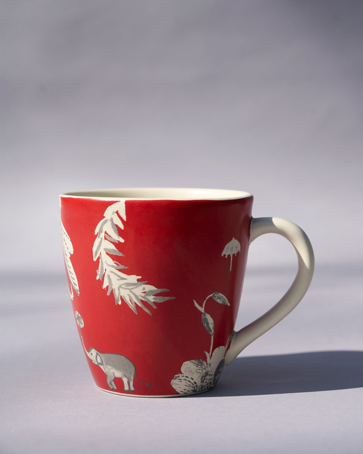 Side view of a red Thazin conical mug with white leaf and elephant motifs.