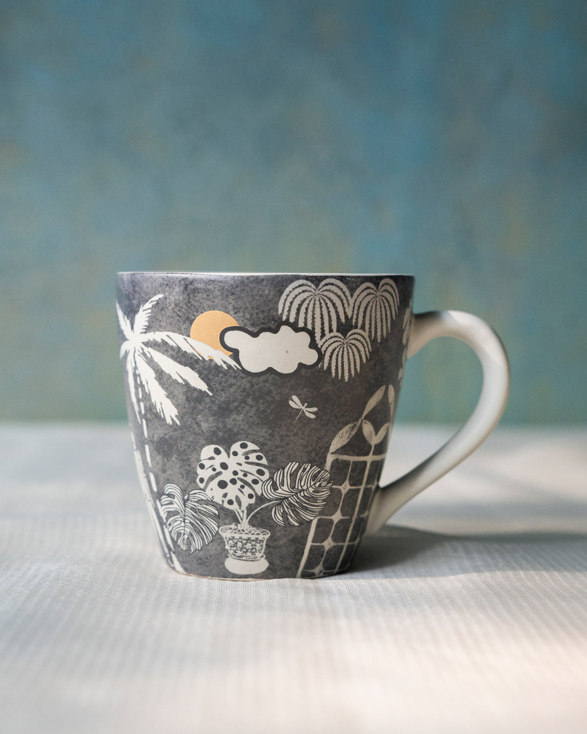 Side view of the Mandovi Palm Mug with a palm, sun and monstera print.
