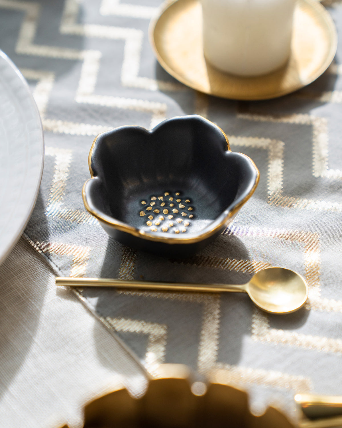 Black Lotus Trinket Tray with a gold rim and dotted centre, beside a gold spoon.