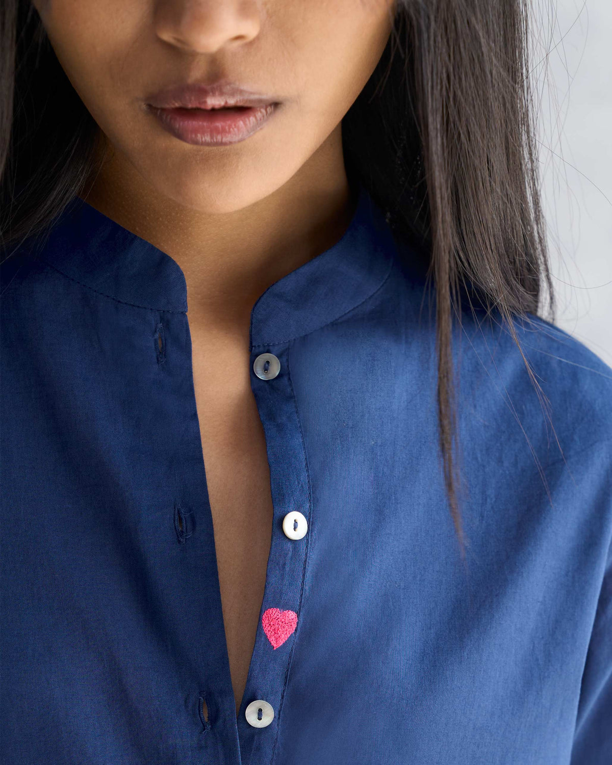 Close-up of a navy mandarin collar top with a small pink heart on the placket.