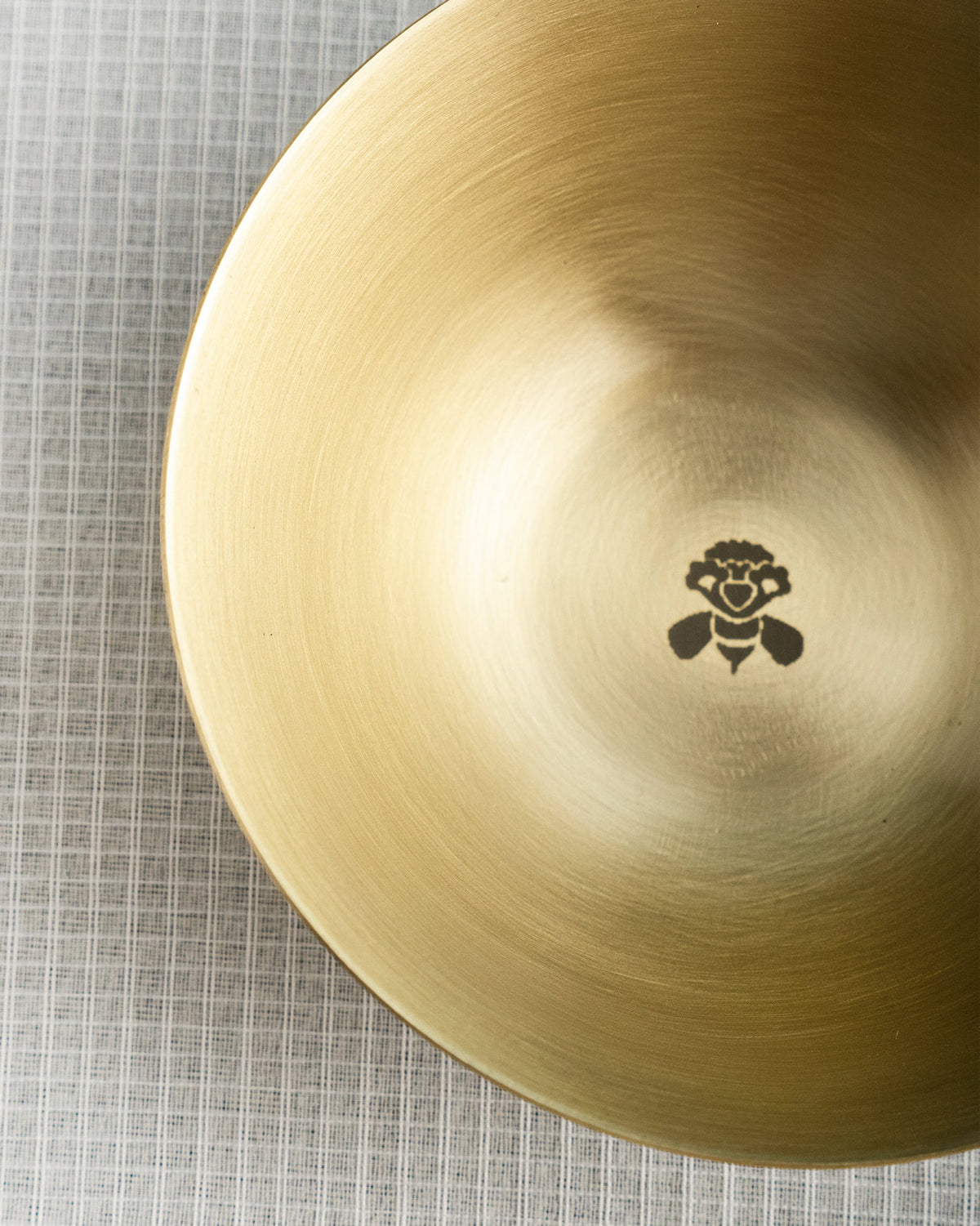 Close-up of a brass Madhu katori showing a small bee motif at the centre.