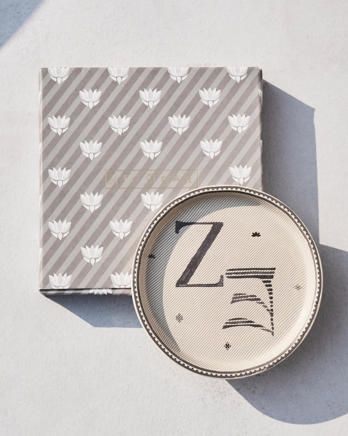 Akshar Coaster - Z resting on its grey lotus-print box.