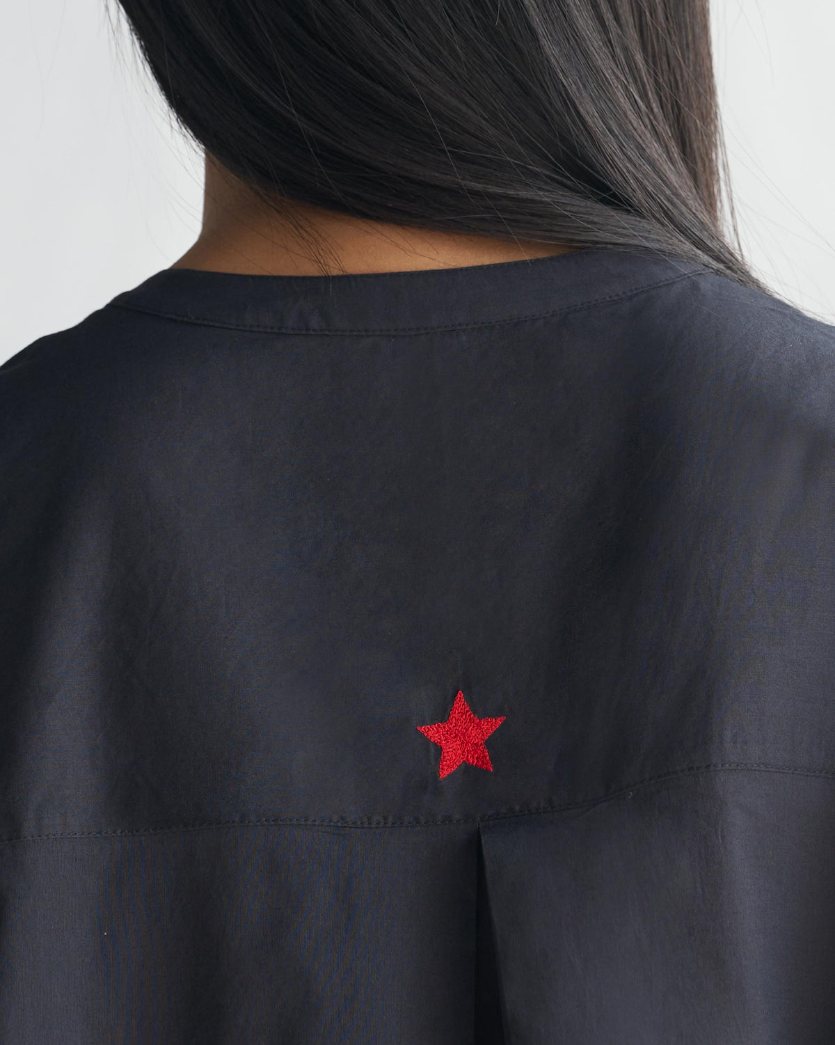 Close-up of a red embroidered star on the back of a black Lazy Sunday tunic.