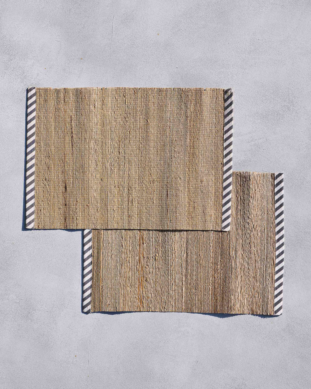 Pair of banana fibre placemats with navy and white striped end borders.