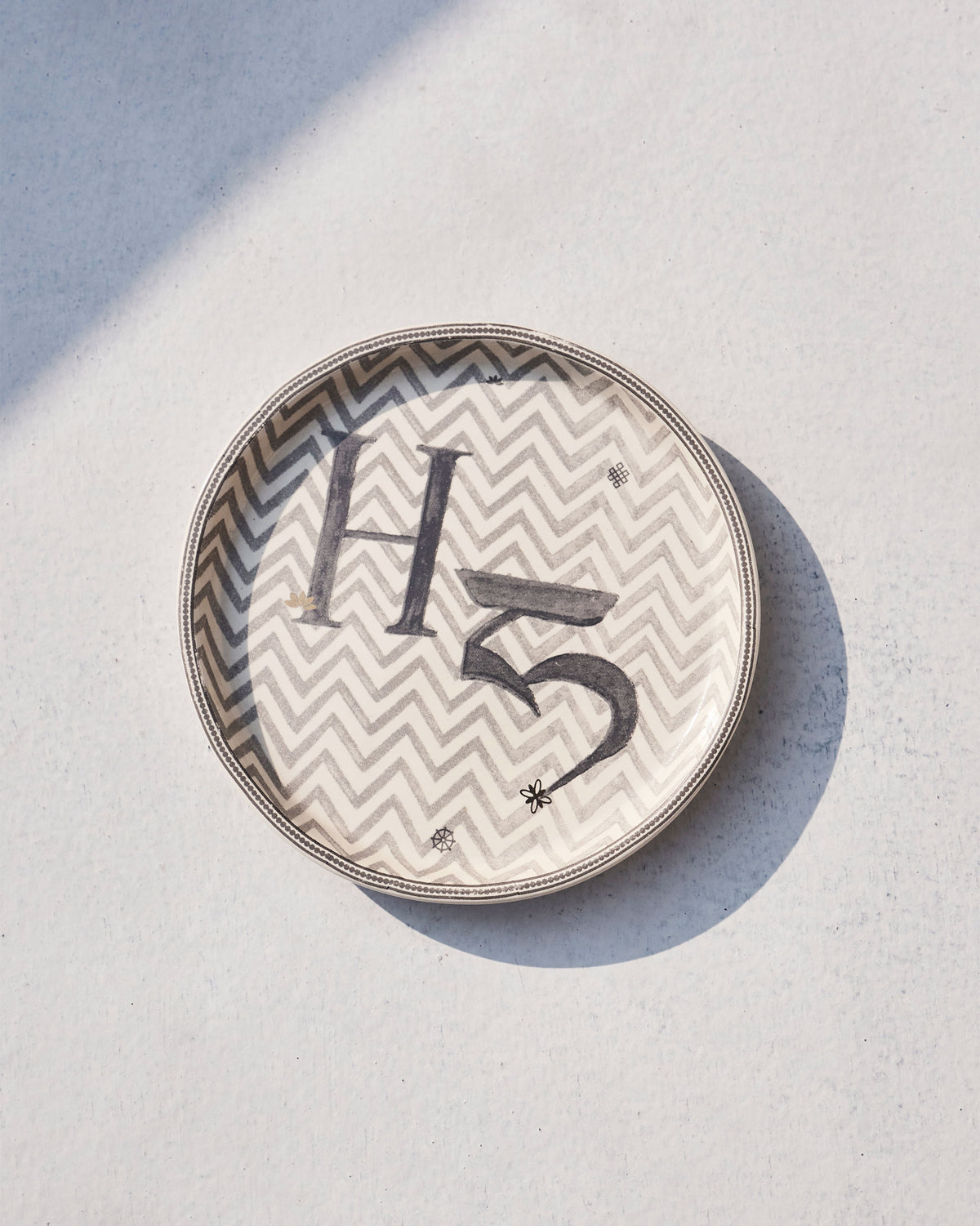 Akshar Coaster with letter H on a grey chevron pattern, slightly angled.