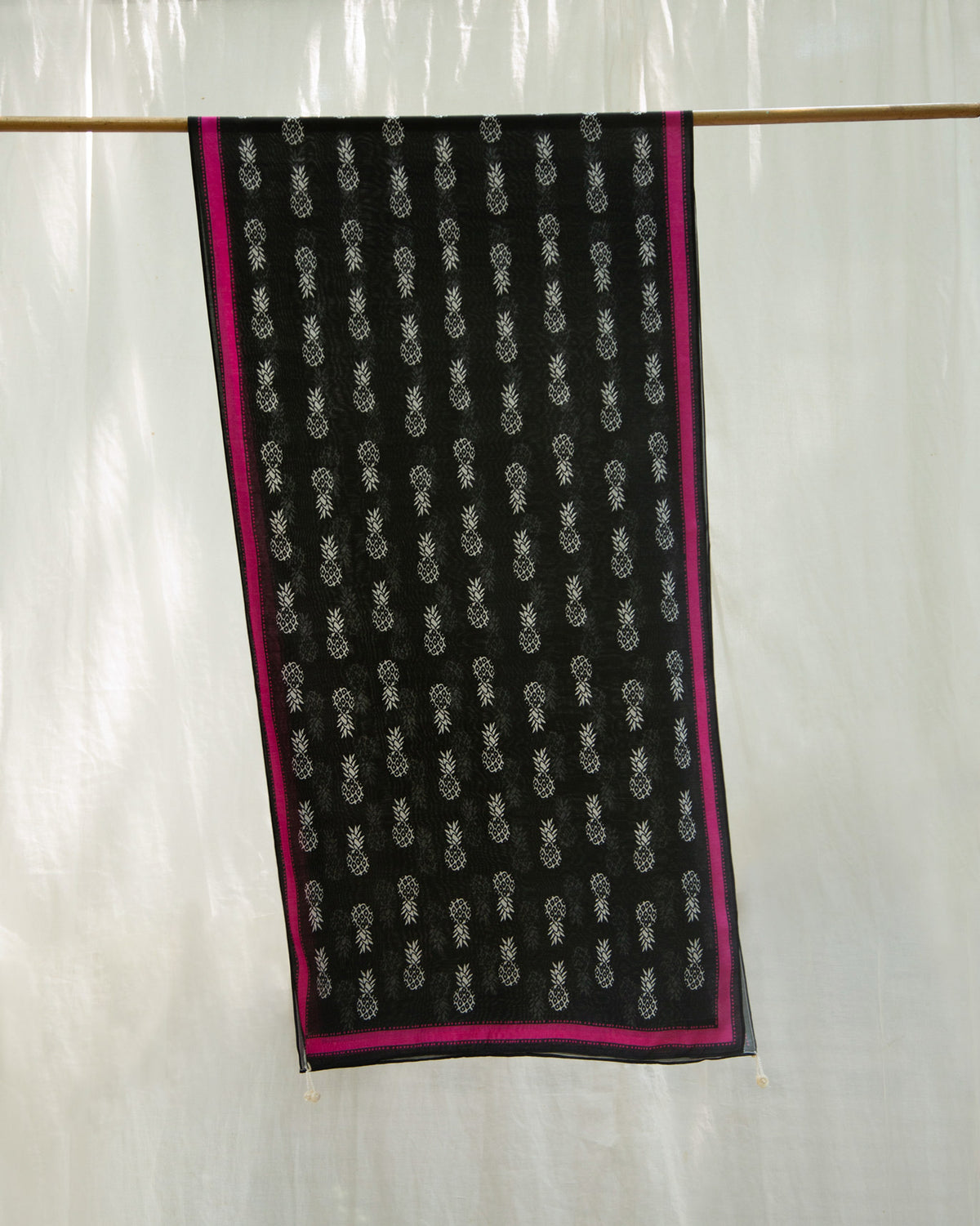 Tropico Scarf in black with pink edges, hung on a rod.