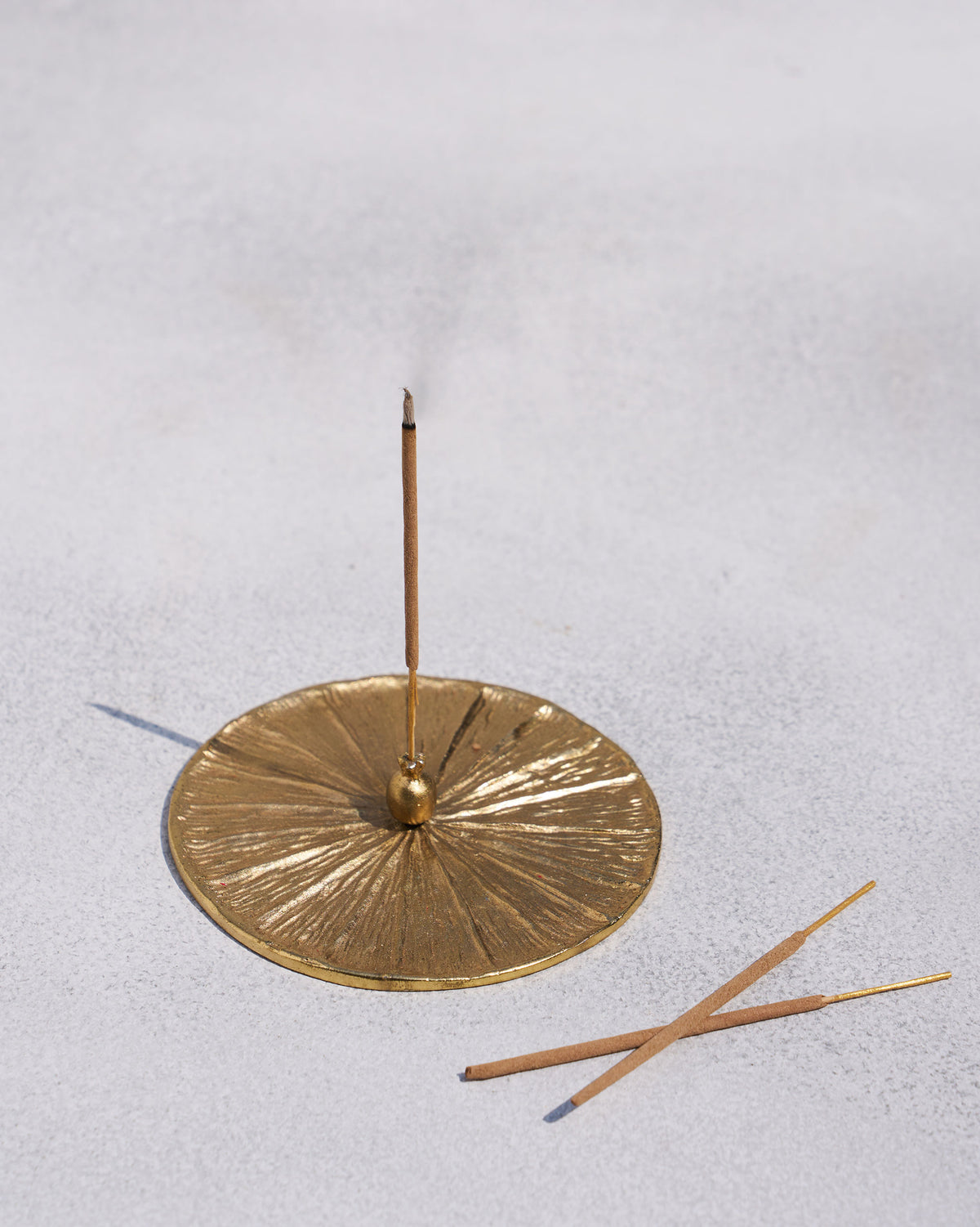 Gold Anar incense holder with a lit stick and two spare sticks beside it.