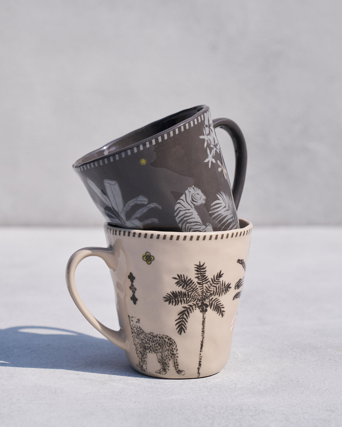 Stacked Malabar conical mugs with leopard, palm, and tiger illustrations.