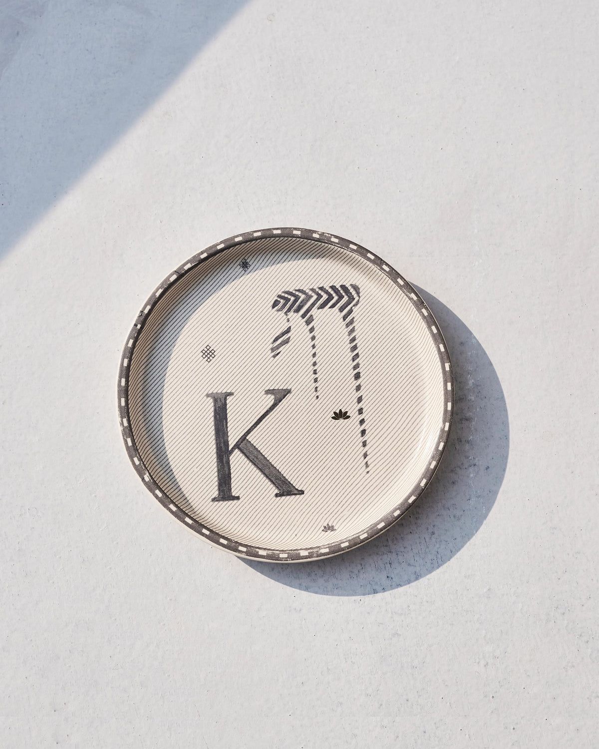 Akshar Coaster with a bold letter K on cream, seen from above.
