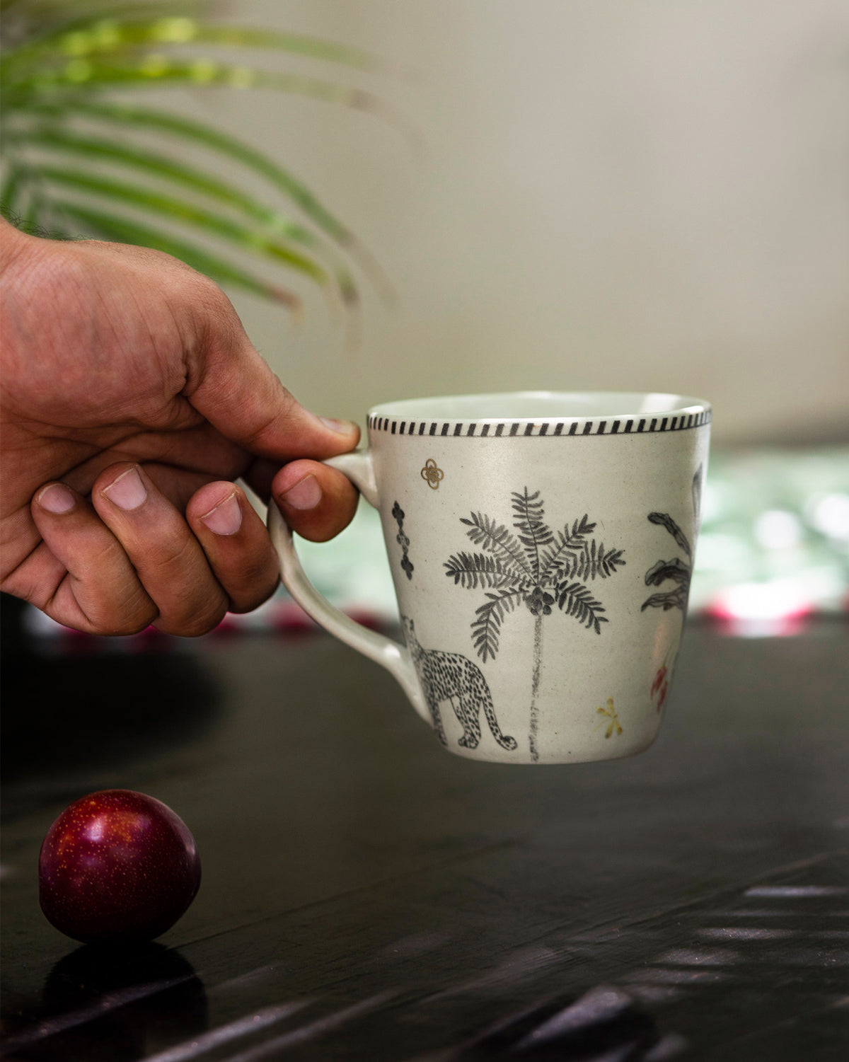 Periyar Mug Ivory held in a hand, showing a palm tree and leopard motif.