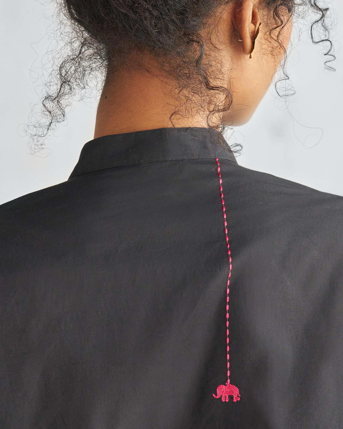 Close-up of pink elephant embroidery on the back of a black mid-length kurta.