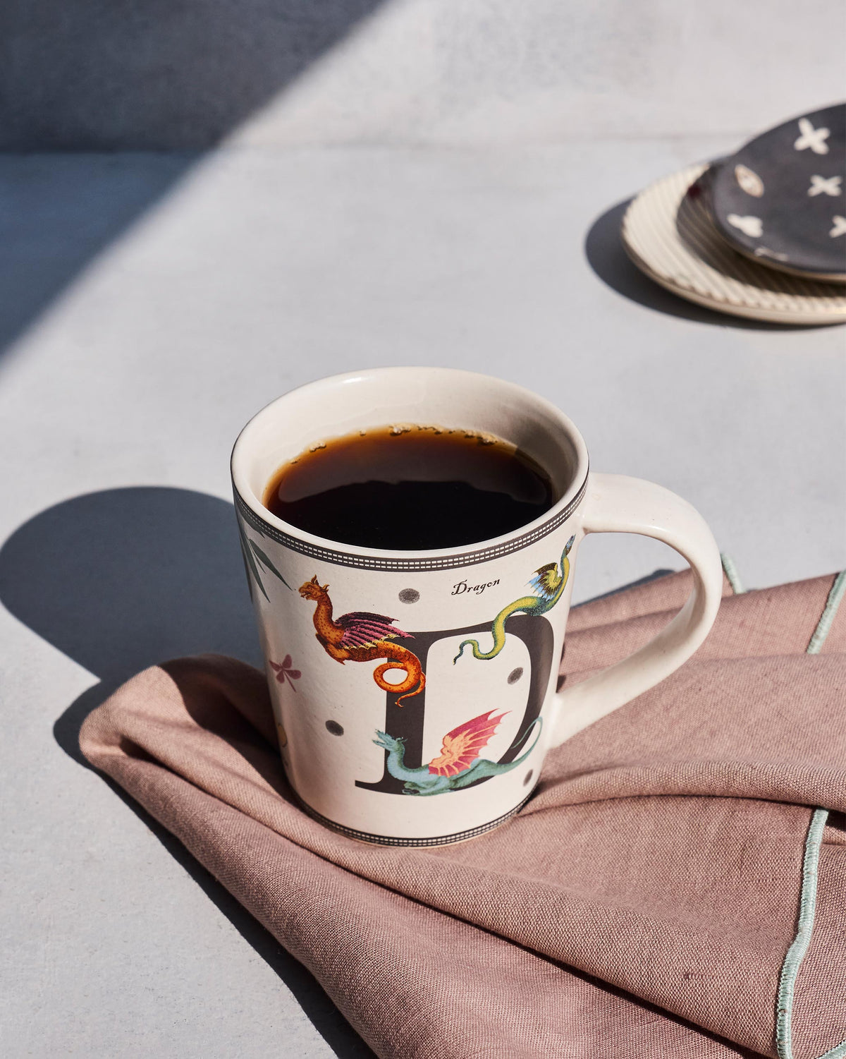 Cream Dariya mug with a letter D and dragon motifs, filled with coffee.