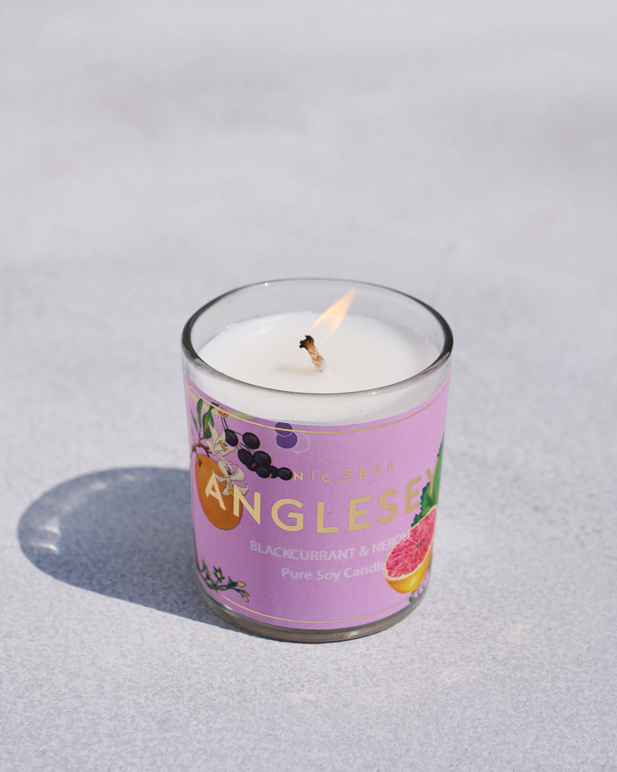 Close-up of a lit Anglesey jar candle with a lilac label.