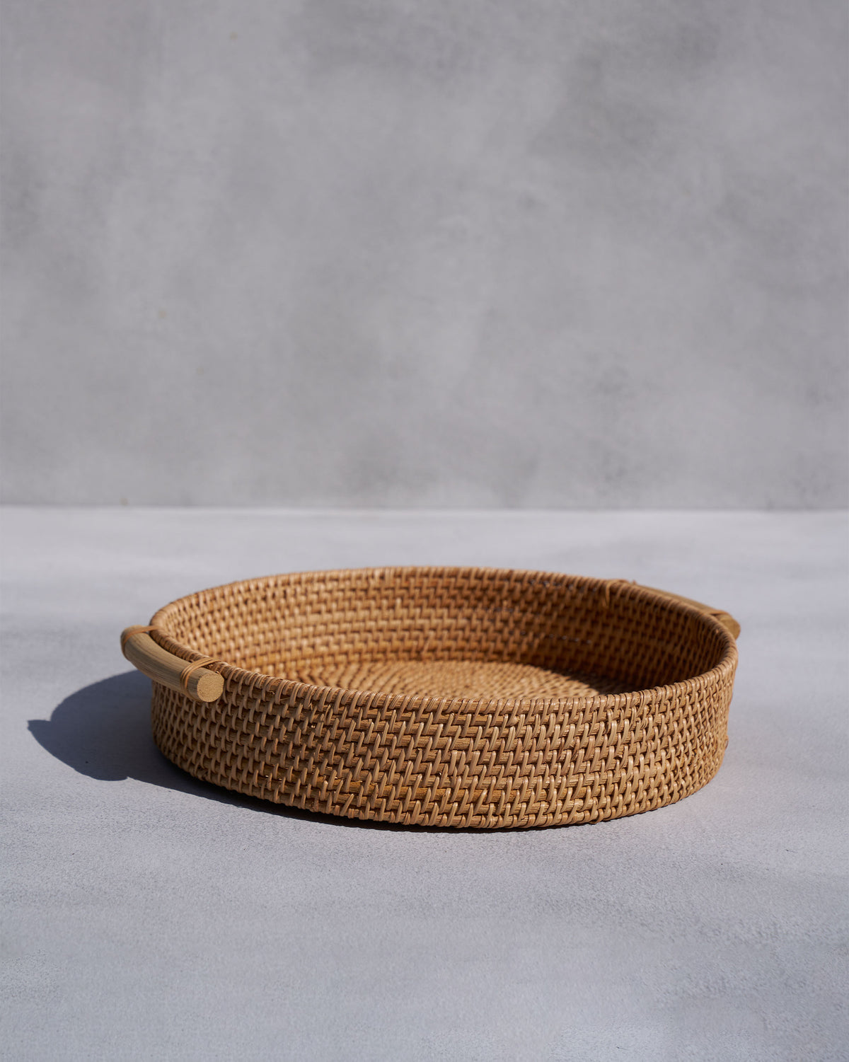 Round woven rattan tray with two wooden side handles.