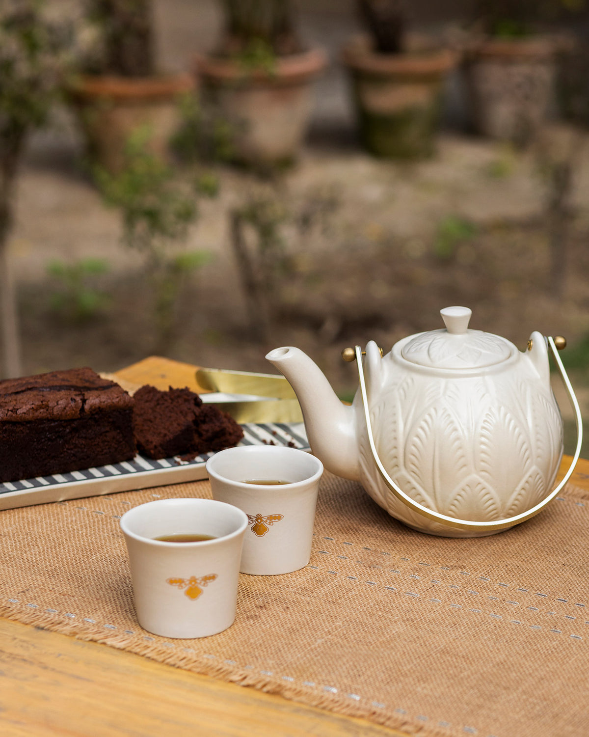 Teesta teapot and teacups with bee motifs beside cake.