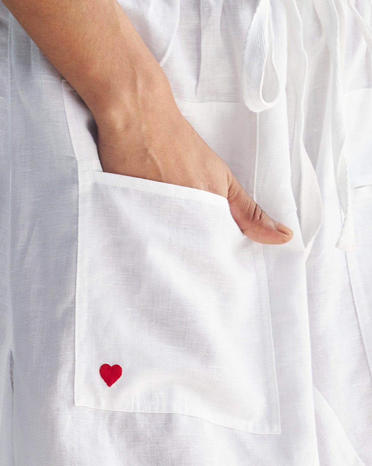 Close-up of white Yoka Trousers pocket with a small red heart embroidered on it.