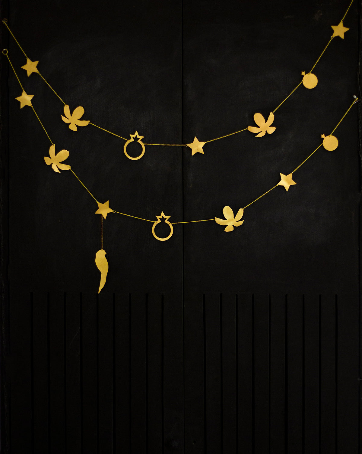 Kachnaar Toran with gold star, flower and ring motifs hanging against black.