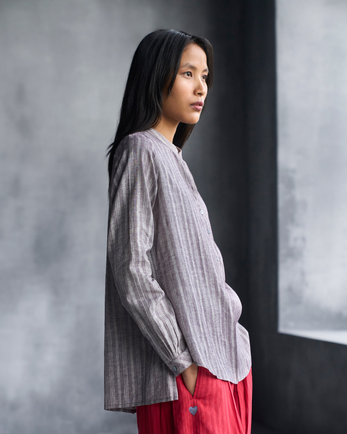 Side view of a grey striped mandarin collar top showing its curved hem.