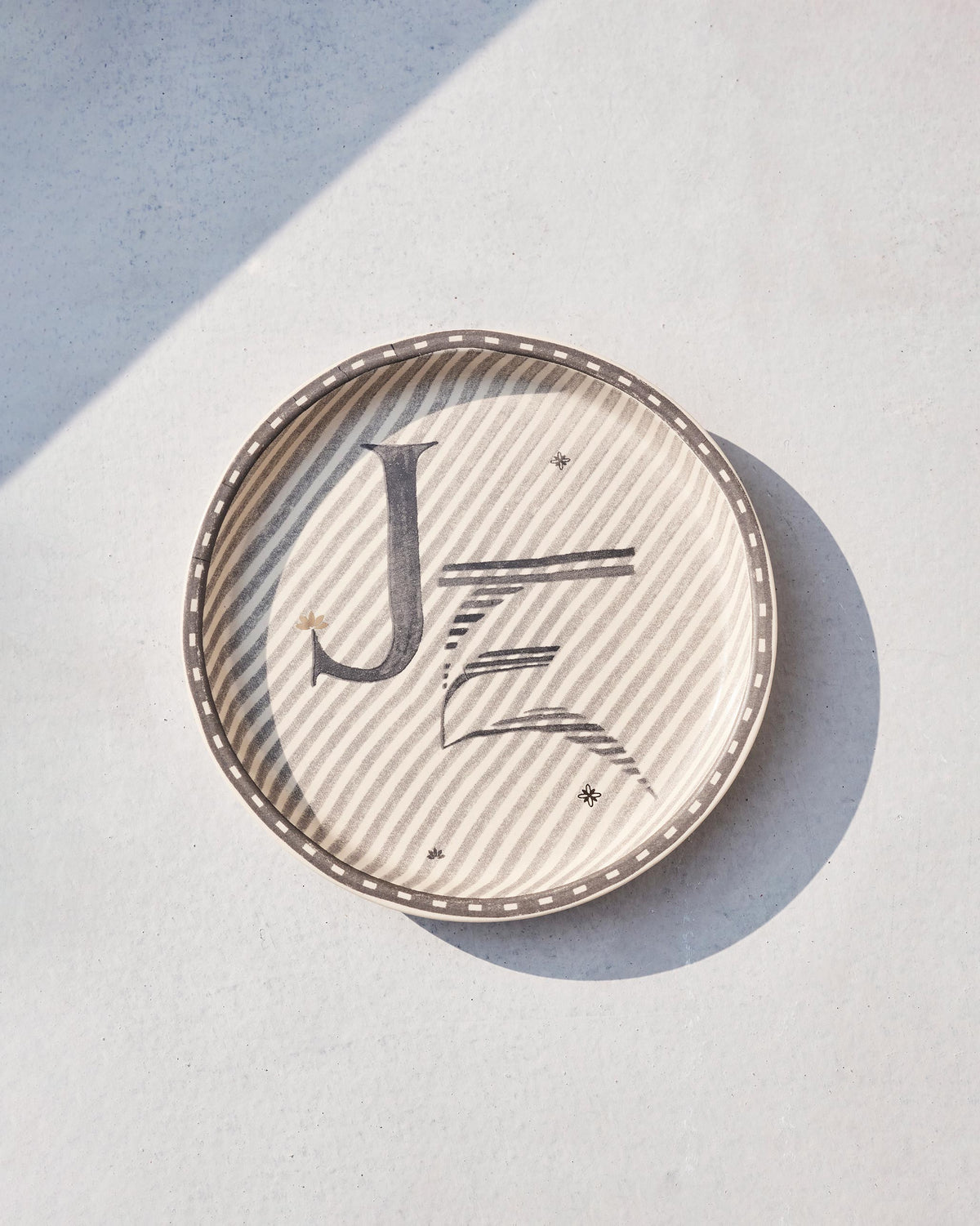 Akshar Coaster with a letter J, slightly angled, showing its beaded rim.
