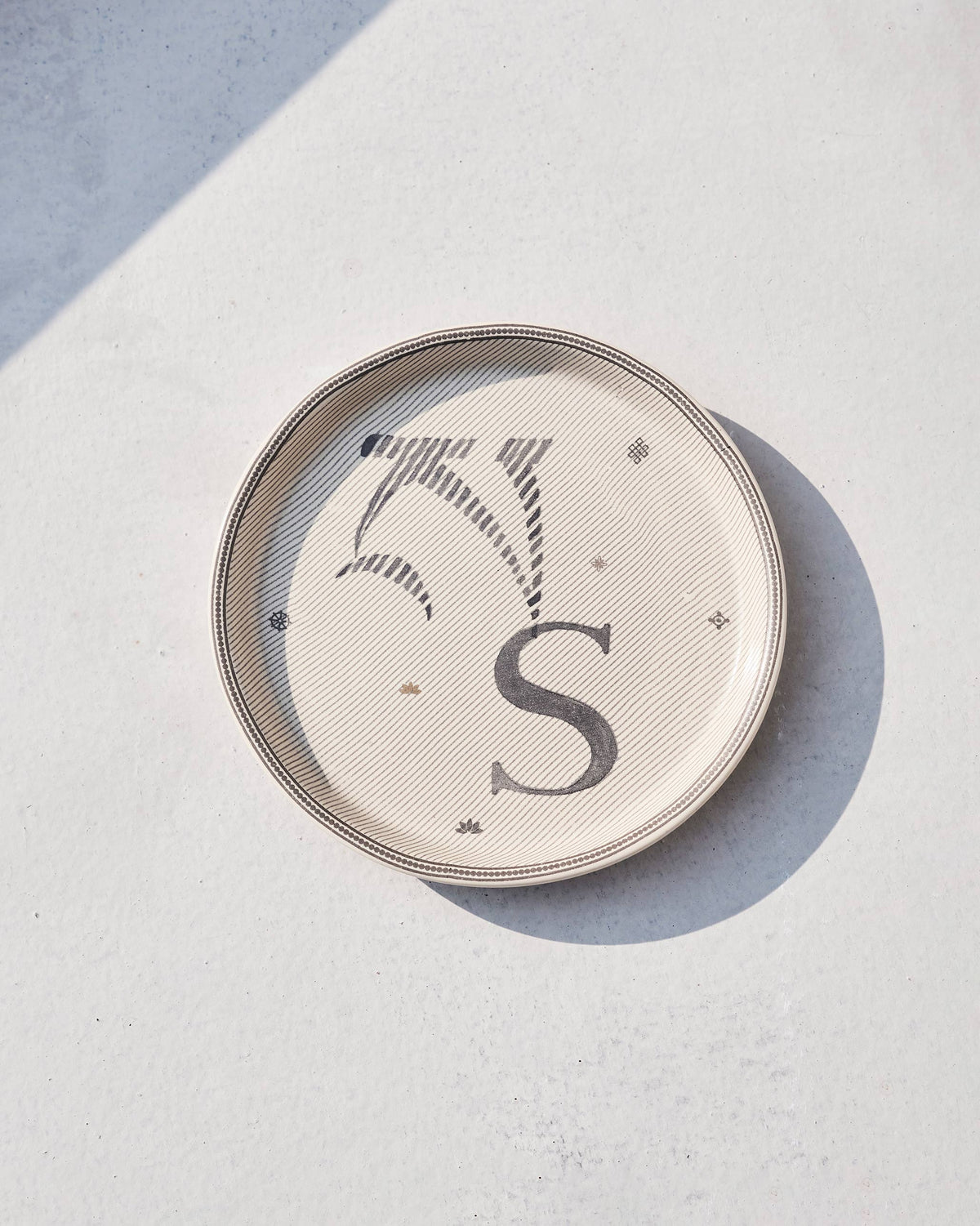 Cream Akshar coaster showing a charcoal letter S on a fine diagonal stripe ground.