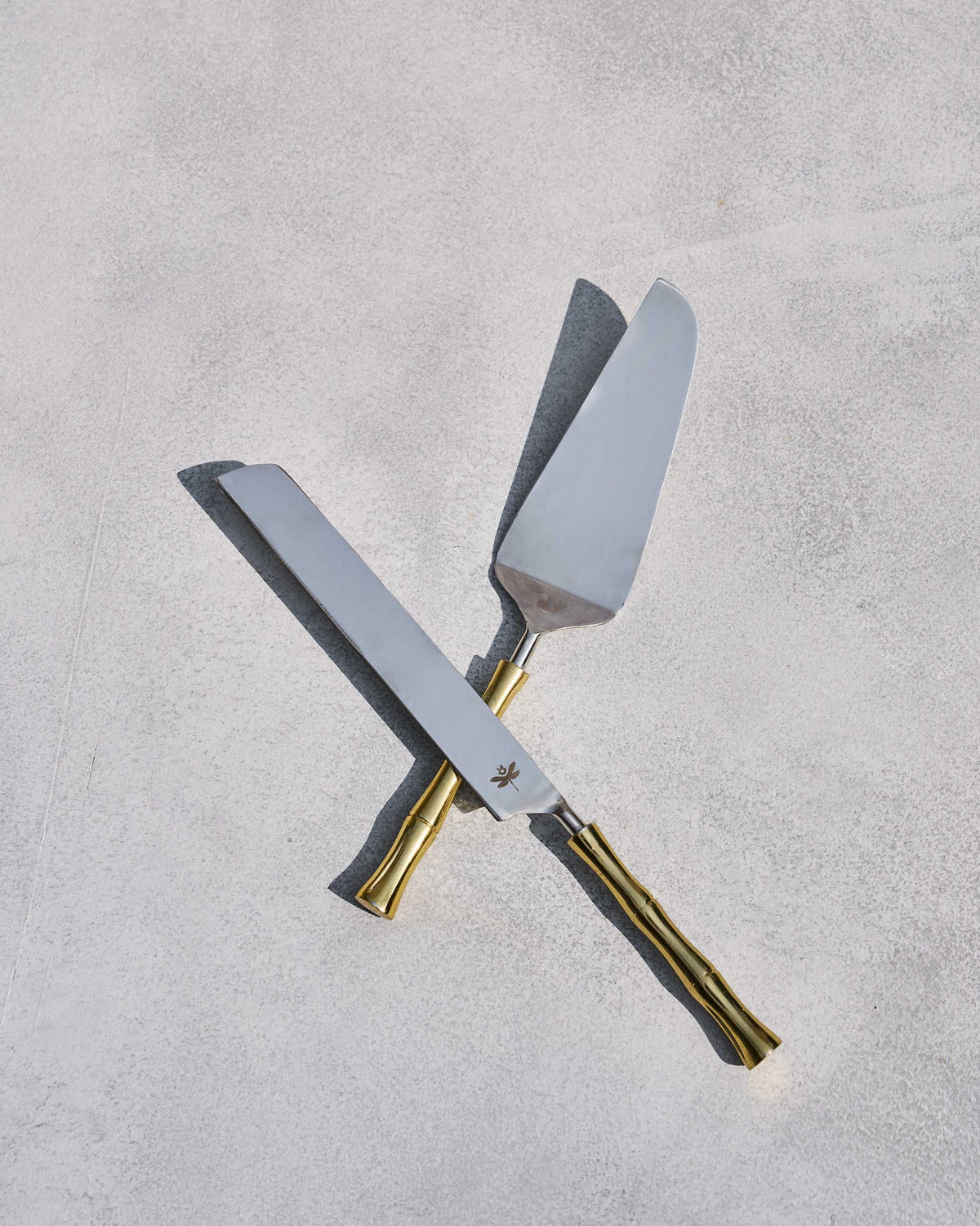 Sunrise cake knife and server crossed on a grey surface.