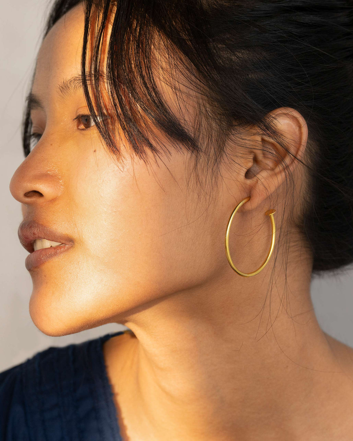 Side profile of a large gold hoop earring showing the back fastening.