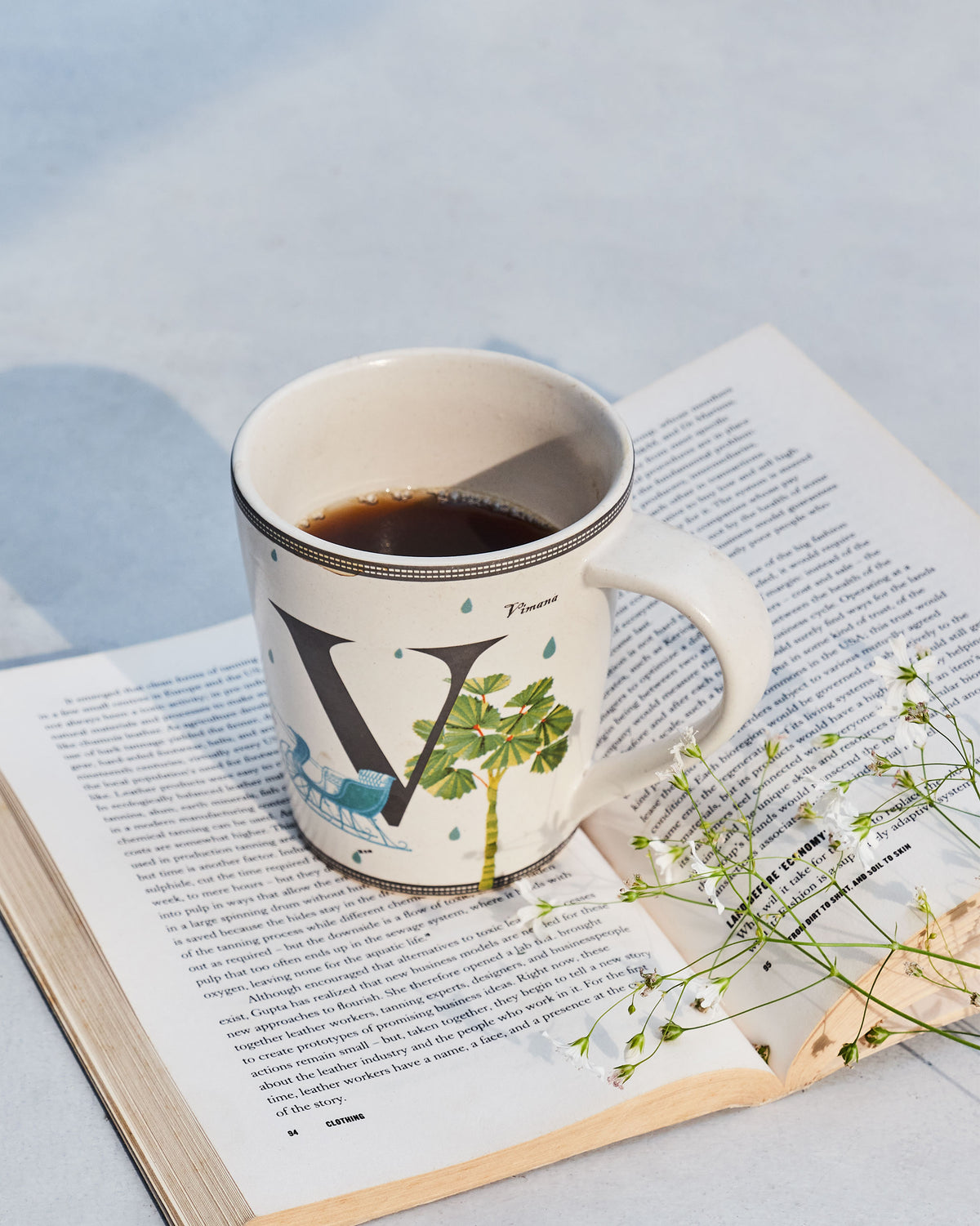 Vriksh mug with a large V and palm print resting on an open book.