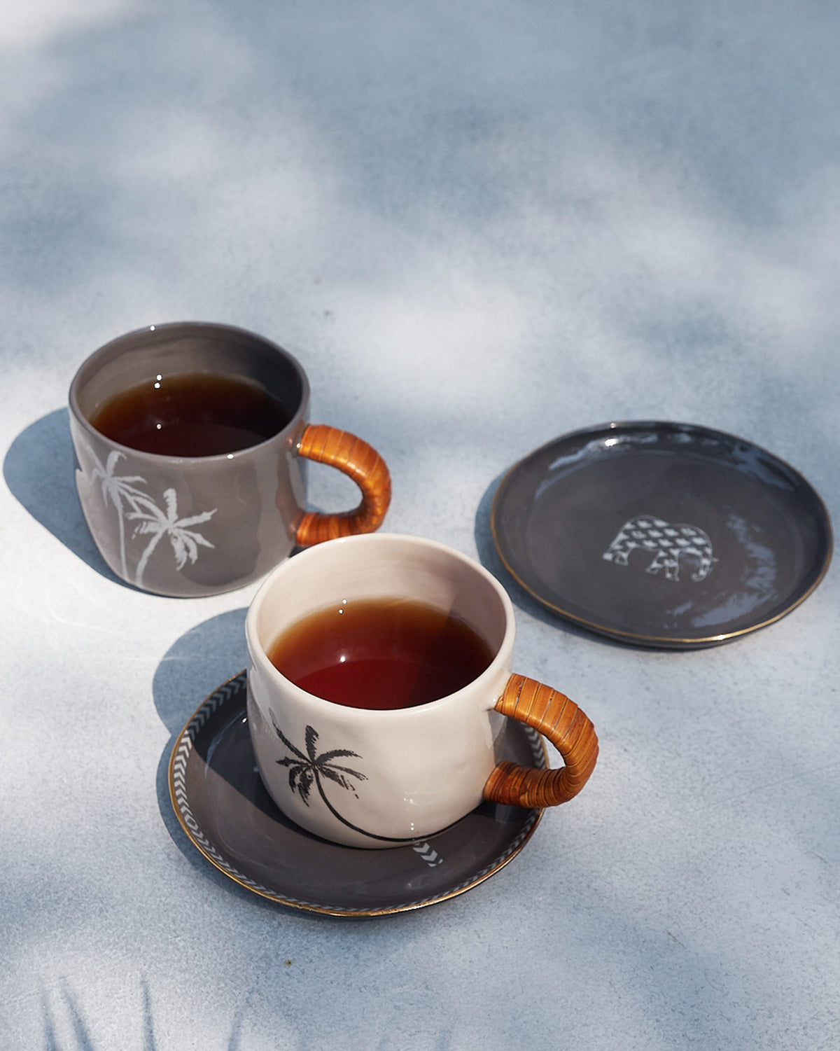 Ivory and charcoal Mandovi mugs with palm motifs and rattan handles.