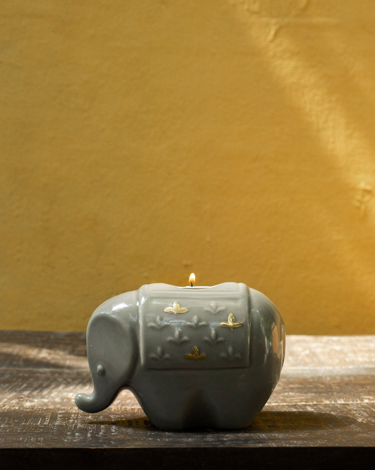 Large Ele votive in grey-green ceramic with a lit candle on top.