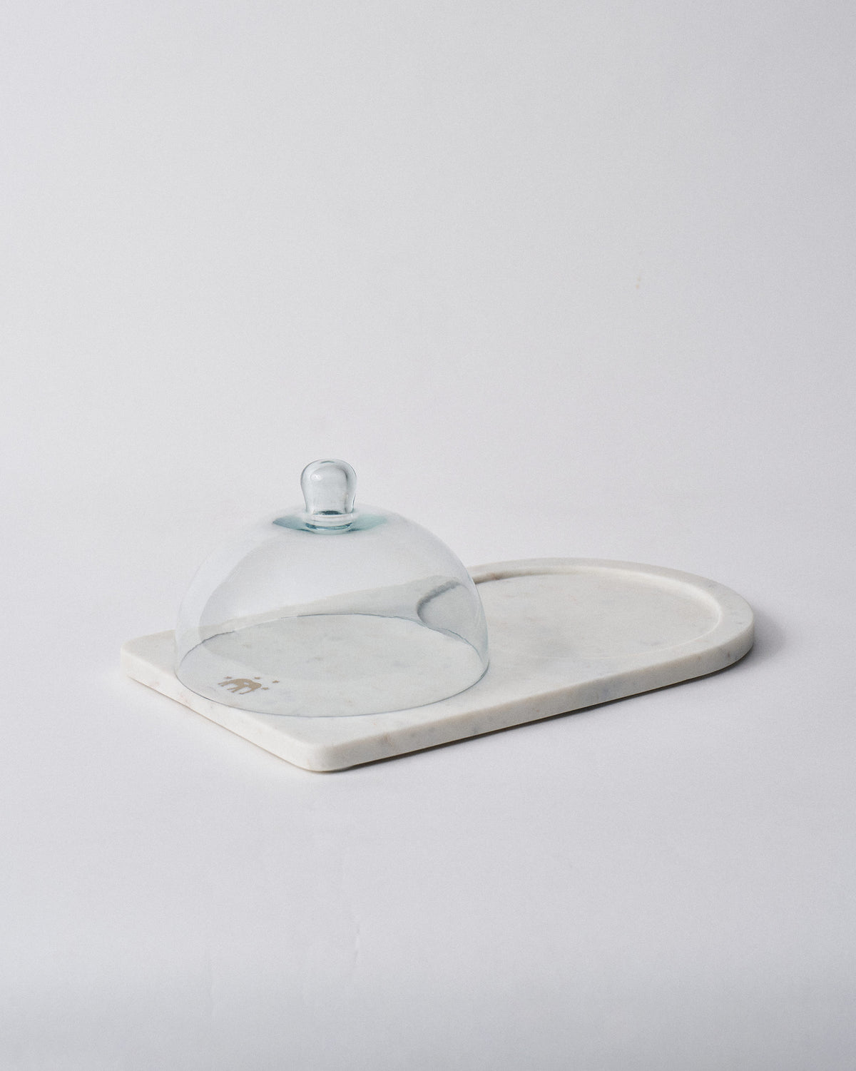 Ele cheese cloche with clear glass dome covering one end of the marble platter.